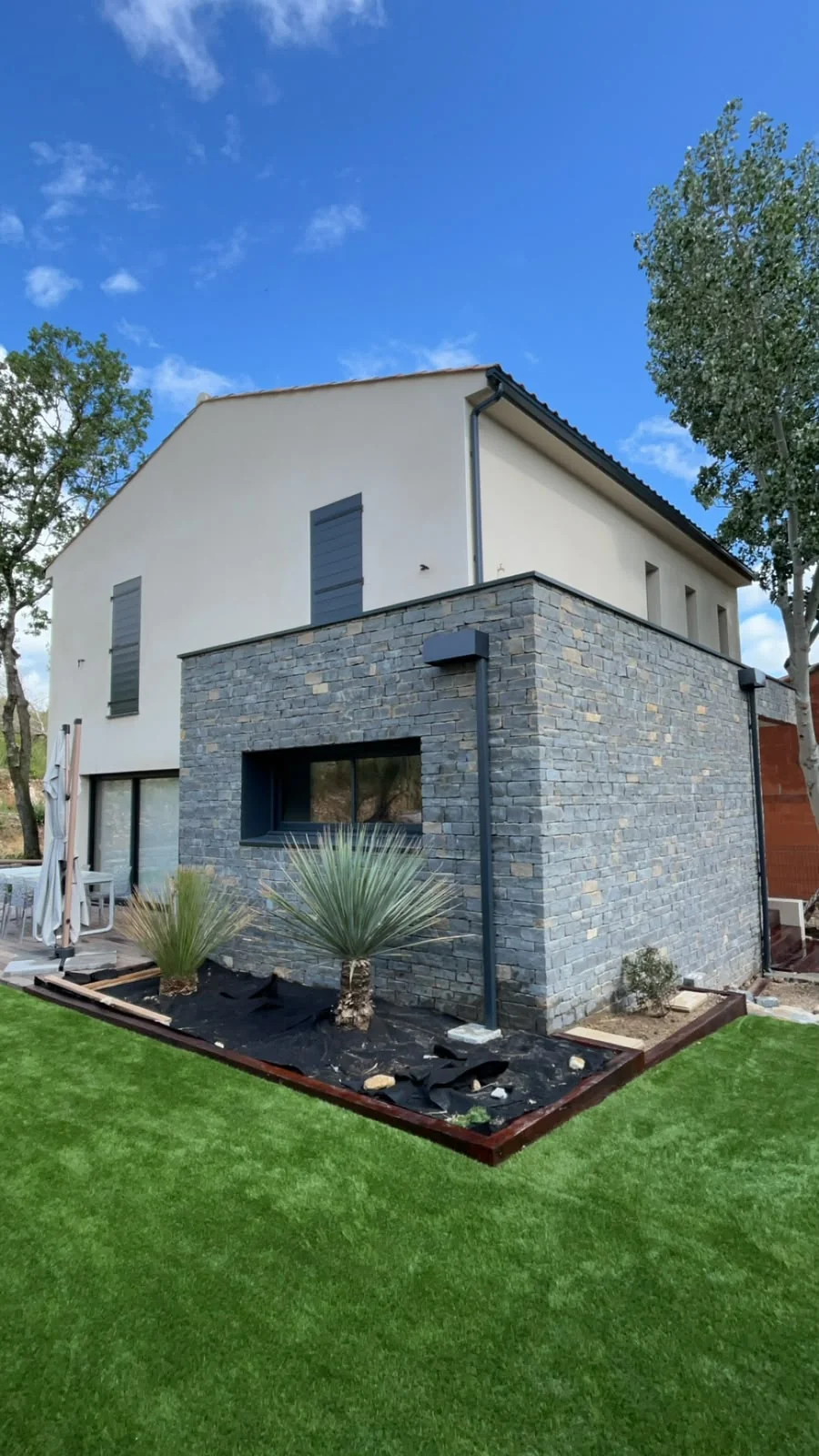 Descente pluviale noire sur une maison moderne avec parement en pierre